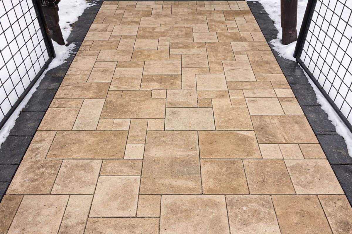 Tan paver patio laid in a mixed pattern between two fences